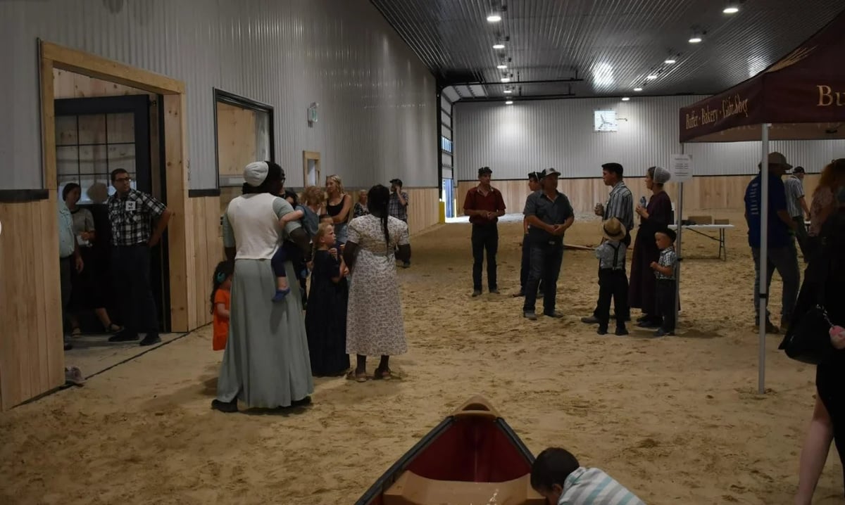 Group of people gathered in an indoor arena with sandy floor, dressed in formal attire during an event.
