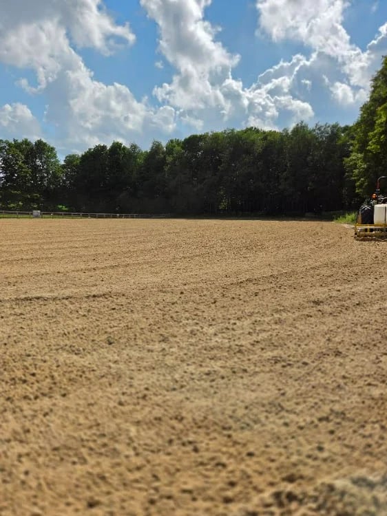 Empty dirt field with tree line in background under partly cloudy blue sky