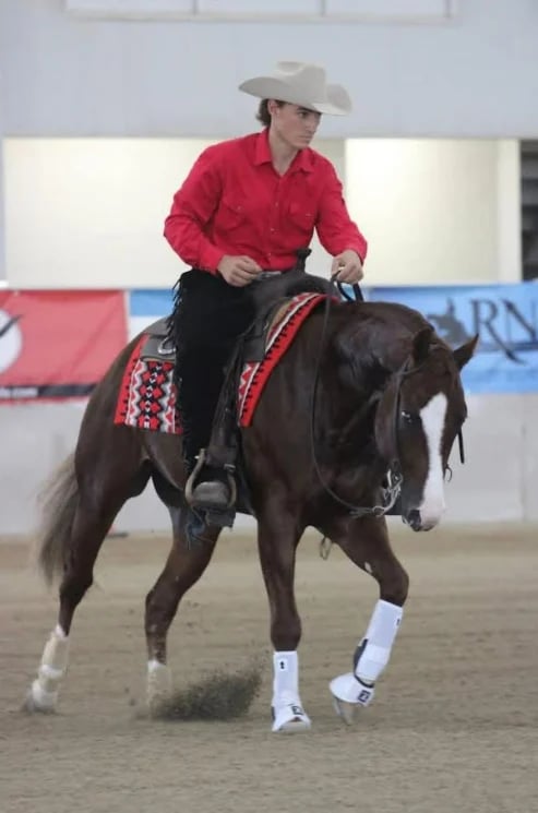 Cowboy in red shirt and hat riding dark brown horse with decorative saddle at indoor arena event